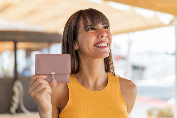 Nuori nainen, jolla on lompakko ulkona katselemassa hymyillen - Valokuva, kuva