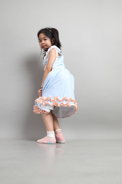 Маленькая порезанная азиатка с модной одеждой, стоящая на сером фоне. - Фото, изображение
