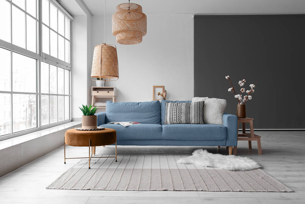 Уютный интерьер гостиной с голубым диваном, пуфом и плетеной лампой потолок - Фото, изображение