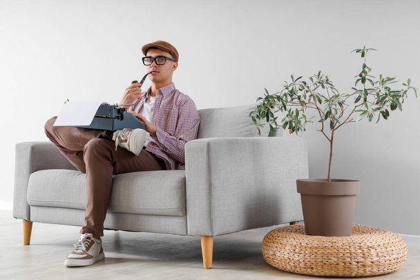 自宅でソファーでヴィンテージタイプライターの喫煙パイプを持つ男性の著者 - 写真・画像