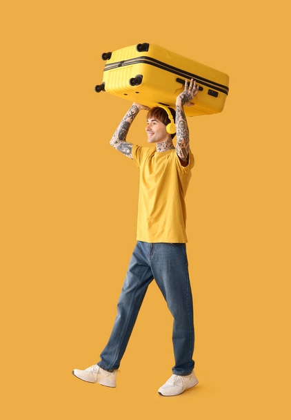 Мужчина турист в наушниках с чемоданом на желтом фоне - Фото, изображение