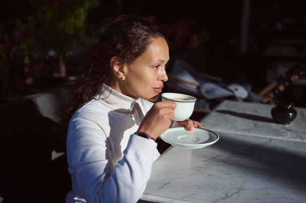 Egy magabiztos, komoly afro-amerikai fiatal üzletasszony portréja, aki egy kávézó kültéri teraszán élvezi forró italát. - Fotó, kép