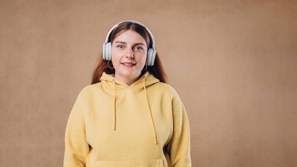 Profil-Porträt einer charmanten Frau mit massiven Kopfhörern, die auf isoliertem Hintergrund Musik hört. Glückliches Mädchen im Kapuzenpulli lächelt. - Foto, Bild