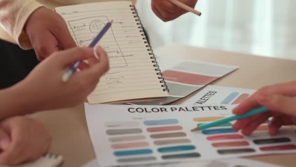 Not defterine yeni tasarım taslağı hazırlayan ve projeyi denetleyen müşteriyle renk seçimi yapan iki tasarımcının yavaş çekim çekimi. Tasarımcı bürosunda kromatik danışma. Değiştirilmiş - Video, Çekim