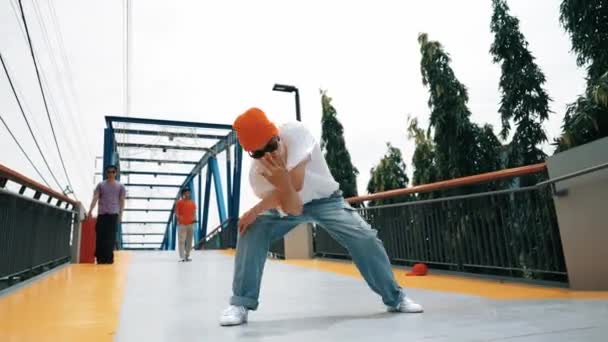 Panorama shot van professionele hipster uit te voeren b-boy prestaties en energieke voetstap. Bekwame gelukkige man oefent breakdance terwijl een vriend hem aanmoedigt op de brug. Outdoor sport 2024. Schitterend.. - Video
