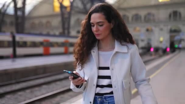 Молодая красивая женщина с помощью смартфона на вокзале - Кадры, видео