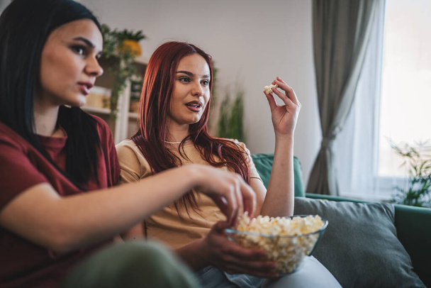 dos mujeres caucásicas adolescentes amigos o hermanas ver película serie de televisión en casa sentarse en el sofá cama con palomitas de maíz - Foto, imagen