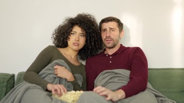Медленное видео мультиэтнической пары, смотрящей фильм ужасов, поедающей попкорн дома - Кадры, видео