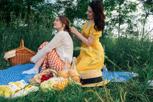 Hair bonding: young woman braids friends hair during picnic - Photo, Image
