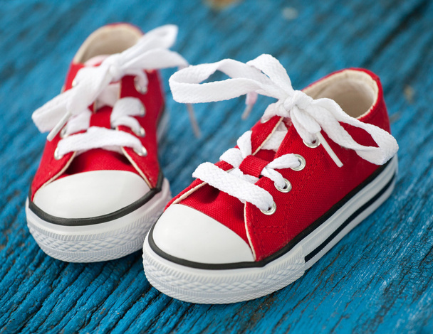 rode baby sneakers op houten blauwe achtergrond - Foto, afbeelding