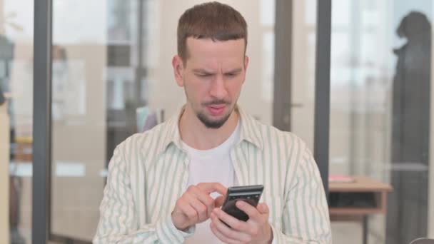 Portrait de jeune homme créatif choqué par la perte au téléphone - Séquence, vidéo