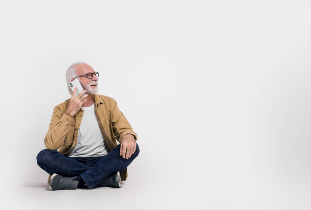 Öreg férfi vállalkozó beszél mobiltelefonon, és félrenéz, miközben ül a fehér háttér - Fotó, kép