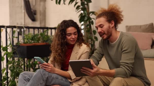 Junge Coworking Coworker treffen sich mit digitalem Tablet, junge kaukasische Frau mit lockigem Haar mit rothaarigem Mann. - Filmmaterial, Video