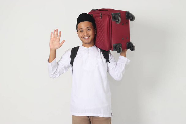 Ritratto di attraente uomo musulmano asiatico che porta la valigia mentre saluta per salutare qualcuno. Vado a casa per Eid Mubarak. Immagine isolata su sfondo bianco - Foto, immagini