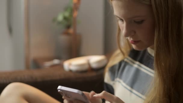 A hipster girl sits in a room, setting aside her phone and picking up a book. The video is taken from the side, capturing the transition from digital interaction to analog engagement,. High quality - Footage, Video
