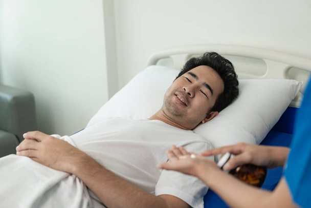An Asian male patient lies in a hospital bed and receives good care from a doctor. Doctor giving advice to male patient working on health diagnosis - Foto, afbeelding