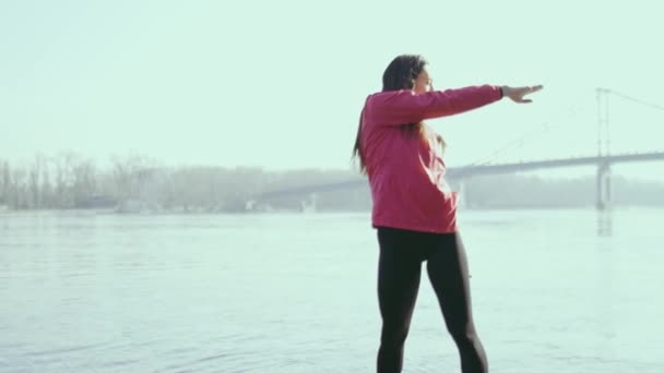 Nuori nainen tekee liikuntaa lähellä jokea - Materiaali, video