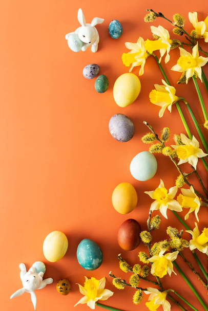 Вид зверху на натуральні барвники пофарбовані великодні яйця на помаранчевому фоні, жовті нарциси та кролики, Щасливий Великдень - Фото, зображення