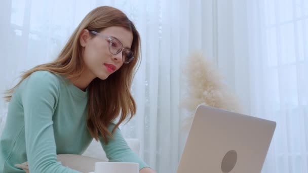 Mladá asijská žena s brýlemi sedící pohovka pracuje na notebooku v obývacím pokoji doma, žena pracuje z domova s domácí práce, na volné noze pracuje na pracovišti, podnikání a digitální život. - Záběry, video