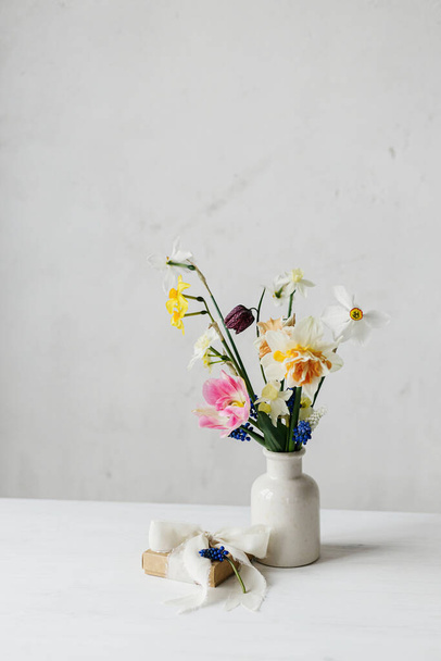 Щасливий жіночий день і день матері. Стильна подарункова коробка зі стрічкою та весняними квітами на сільському білому столі. Красиві нарциси і тюльпани ніжний букет і подарунок. Простір для тексту - Фото, зображення