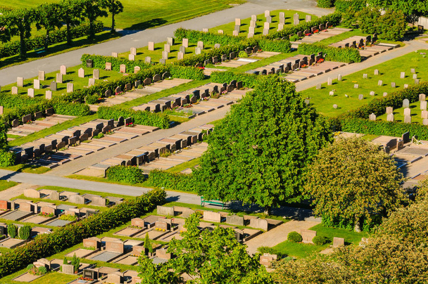 Widok z lotu ptaka oddaje cmentarz położony w parku, z rzędami nagrobków i drzew otaczających teren. Cmentarz w Szwecji można zobaczyć w tle. - Zdjęcie, obraz
