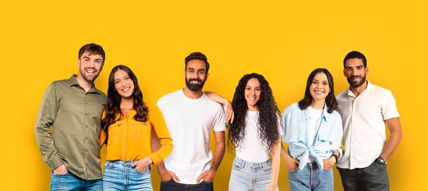 Cinq amis joyeux étudiants avec des tenues décontractées souriants et debout à proximité, mettant en valeur la diversité et l'unité sur fond jaune moutarde, panorama, studio. Étude, éducation - Photo, image