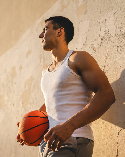 jeden młody kaukaski mężczyzna mężczyzna atleta stoją na zewnątrz trzymać koszykówka piłka nosić biały zbiornik top a-shirt silny umięśniony prawdziwa osoba kopia przestrzeń szczęśliwy uśmiech pewny zdrowy styl życia koncepcja - Zdjęcie, obraz