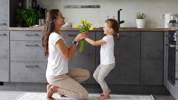 Niña dando flores amarillas a su madre en la cocina del hogar. Día de la madre, cumpleaños o Día Internacional de la Mujer 8 concepto de marzo. Imágenes de alta calidad 4k - Metraje, vídeo