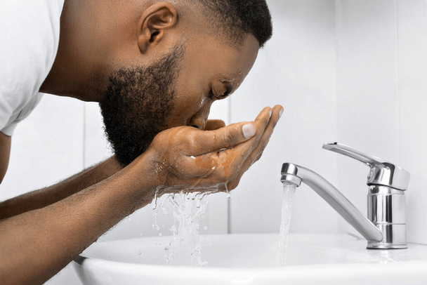 Joven hombre afro lavándose la cara en el baño, espacio para copiar
 - Foto, imagen