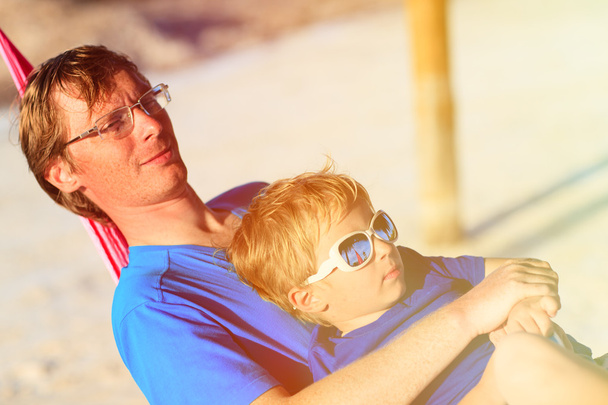 Nuori isä ja pieni poika rentouttava riippumatossa
 - Valokuva, kuva
