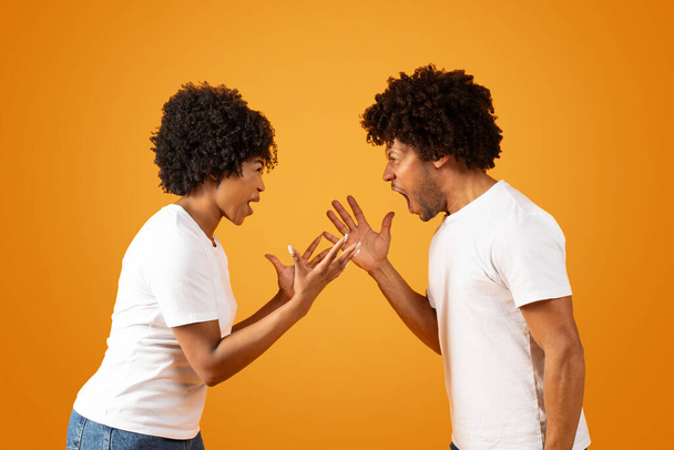 Dühös, ezeréves afro-amerikai férfi és nő pár férj és feleség kiabálnak egymással, gesztikulálnak, házastársak harcolnak elszigetelt narancs alapon. Kapcsolati konfliktusok - Fotó, kép