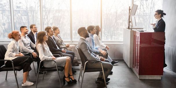 Corporate Training Konzept. Business-Coach hält Präsentation vor jungen Mitarbeitern im Konferenzraum, Seitenansicht - Foto, Bild