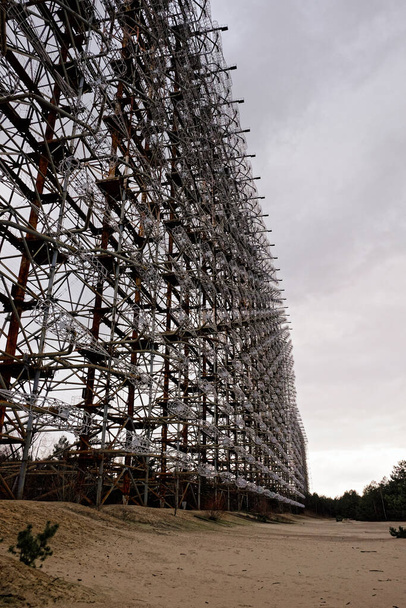 Temidden van droog gras, een ingewikkelde metalen toren strekt zich uit in de lucht met gedetailleerde engineering werk. Duga is een Sovjet over de horizon radarstation voor een vroegtijdig detectiesysteem voor ICBM lanceringen. - Foto, afbeelding