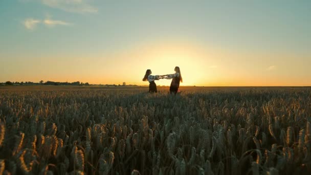 Auringonlasku tanssi vehnäpellolla Kaksi tyttöä, kaksi naista perinteisessä puvussa tanssivat iloisesti vehnäpellolla auringonlaskun aikaan. - Materiaali, video