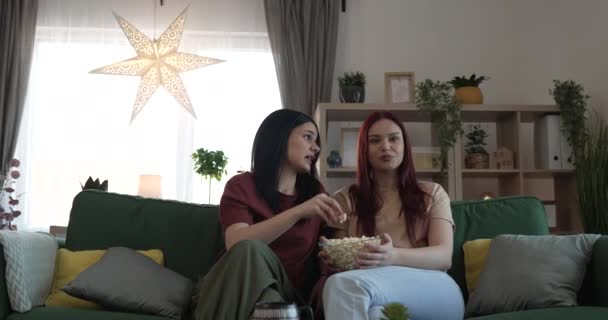 two women caucasian teenage friends or sisters watch movie tv series at home sit on sofa bed with popcorn - Footage, Video