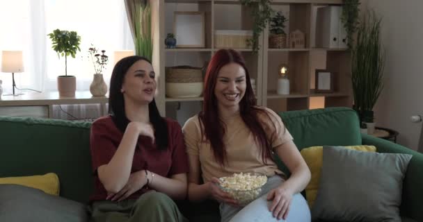dos mujeres caucásicas adolescentes amigos o hermanas ver película serie de televisión en casa sentarse en el sofá cama con palomitas de maíz - Metraje, vídeo