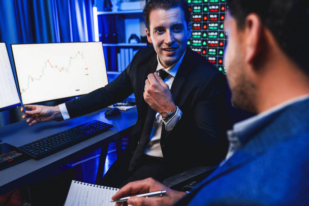 Two stock exchange traders discussing on dynamic investment graph, trending of high profit in currency stock. Showing financial benefit data on monitor screen in neon light at workplace. Sellable. - Photo, Image