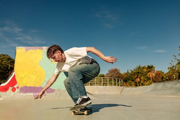 Full body of young male skater in casual outfit doing trick on skateboard riding in skate park - Foto, afbeelding