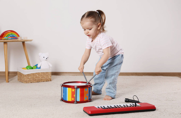 Cute little girl playing with drum, drumsticks and toy piano at home - Foto, Imagen