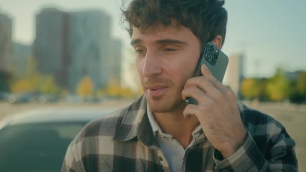 Usmívající se chlap hezký 30s Kavkazský muž řidič mluvit mobilní telefon s auto auto pozadí na parkoviště šťastný muž úspěšný podnikatel volání smartphone přátelský konverzace ve městě městský životní styl - Záběry, video