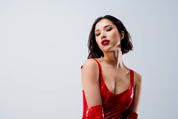 Φωτογραφία από ελκυστική νεαρή γυναίκα δείχνουν στήθος κλειστά μάτια ντυμένα κόκκινα δερμάτινα ρούχα που απομονώνονται σε ανοιχτό γκρι φόντο. - Φωτογραφία, εικόνα