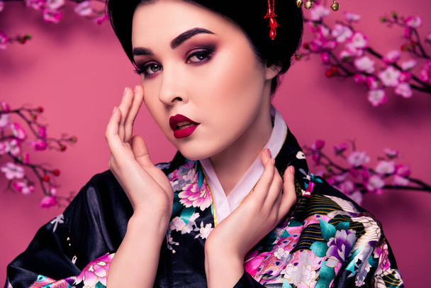 Portrait of gorgeous asian woman in traditional costume showing her perfect make up isolated on pink color background. - Photo, Image