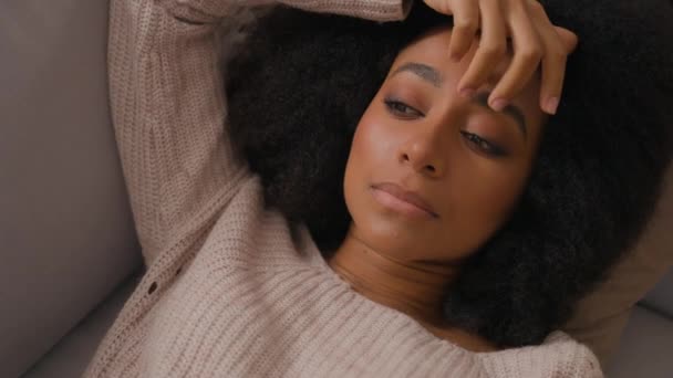 Samotna smutna Afroamerykanka leżąca samotnie na kanapie w domu nieszczęśliwa apatyczna zmęczona leniwa dziewczyna kobieta relaksująca się na sofie depresja cierpiąca na zaburzenia psychiczne - Materiał filmowy, wideo