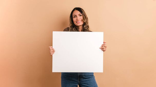 Fondo marrón de una mujer sosteniendo un panel en blanco mientras sonríe a la cámara - Foto, Imagen