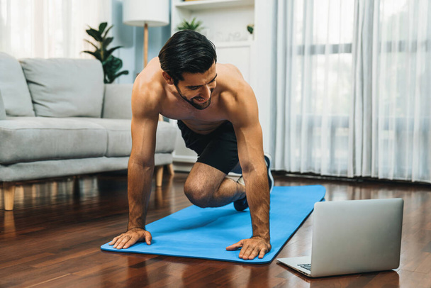 Atletische en sportieve man die bergbeklimmer doet op een fitnessmat tijdens online lichaamsbeweging sessie voor fit lichaamsbouw en gezonde sport levensstijl thuis. Gaiety thuis oefening training. - Foto, afbeelding