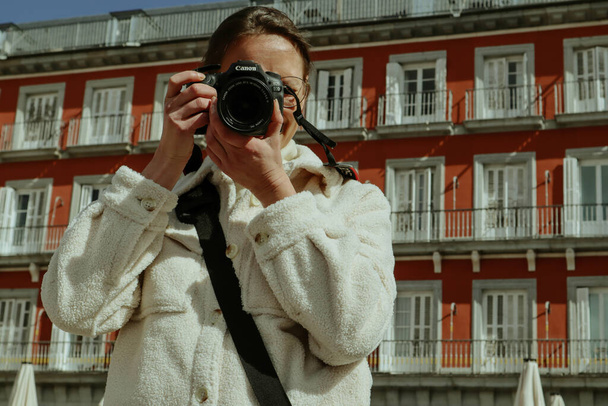 Madrid, Spanien. 27. Februar 2024 Eine Touristin macht ein Foto von einer Plaza Mayor, die die spanische Hauptstadt besucht. Reisefotograf. Roter Altbau. - Foto, Bild