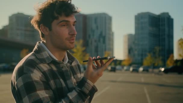 młody przystojny mężczyzna kaukaski facet spacery w mieście nagrywanie wiadomości głosowych na smartfonie online czat odkryty pozytywny uśmiech millennial wysyłanie audio poczta głosowa rozmawianie z telefon komórkowy głośnik - Materiał filmowy, wideo