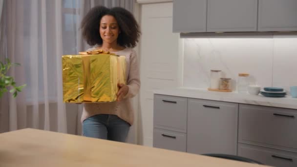 Feliz sonriente mujer afroamericana comprador chica obtener entrega caja grande regalo de cumpleaños desembalaje paquete de papel dorado unbox paquete de apertura orden de compra de regalo de la tienda en línea servicio de envío - Imágenes, Vídeo