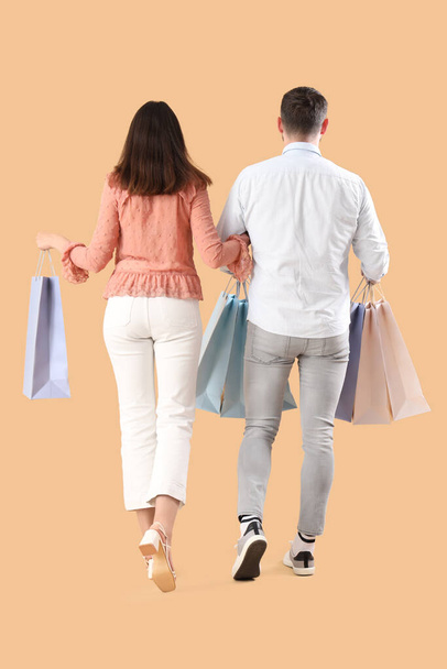 Feliz pareja joven con bolsas de compras sobre fondo beige, vista trasera - Foto, Imagen