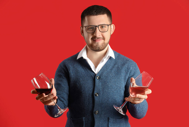 Sommelier joven sosteniendo copas con diferentes tipos de vino sobre fondo rojo - Foto, imagen